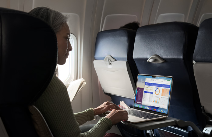Une personne assise dans un avion travaille sur son MacBook Air