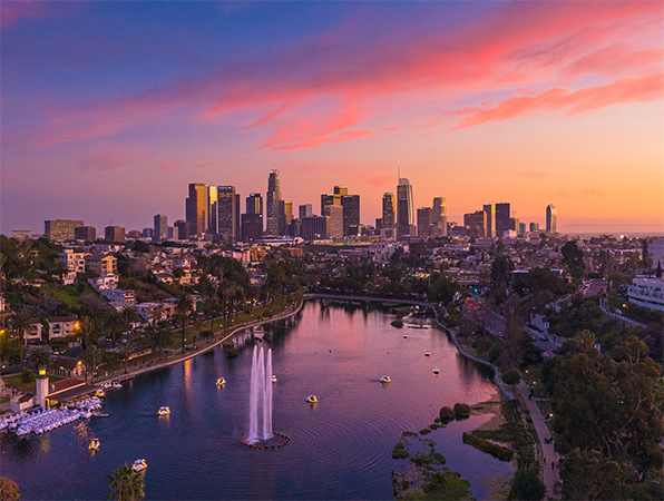 Aerial view looking toward Los Angeles skyscrapers with a park and a lake in the foreground.