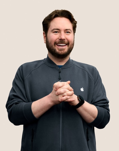 Portrait of a smiling Apple Retail team member with short, wavy dark hair and a beard.