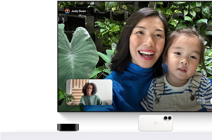 Apple TV 4K et iPhone : l’écran de télévision affiche un appel FaceTime, une personne porte une fillette, la personne ayant initié l’appel apparaît dans une fenêtre incrustée