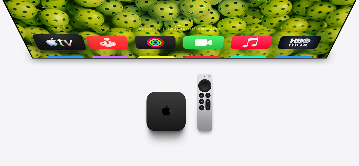 Une Apple TV 4K et une télécommande Siri Remote sous un écran de télévision, l’écran affiche la rangée supérieure des icônes d’apps de l’écran d’accueil sur un fond vert de pickleball