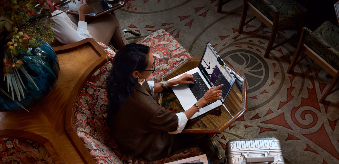 공공 공간의 테이블에 앉아 있는 사람이 핀치 제스처로 PROLED XDR 디스플레이 탑재 MacBook Pro 실버 모델의 터치 기능을 통해 Xcode에서 요소를 조절하는 모습. 테이블의 노트북 옆에는 iPhone이 놓여 있고, 해당 인물이 AirPods Pro를 사용 중입니다.