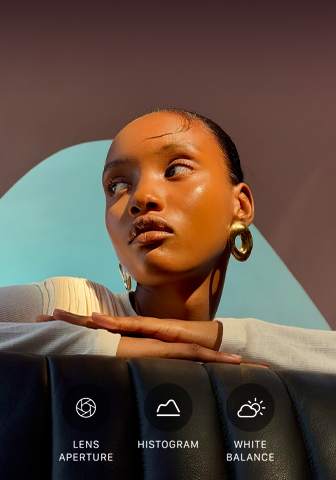 Portrets tuvplānā ar labi izgaismotu modeli uz krāsaina fona, kurā demonstrē pro kameru sistēmas Pro vadības rīkus: diafragmas atvērumam, histogrammas apskatei, baltā līdzsvaram