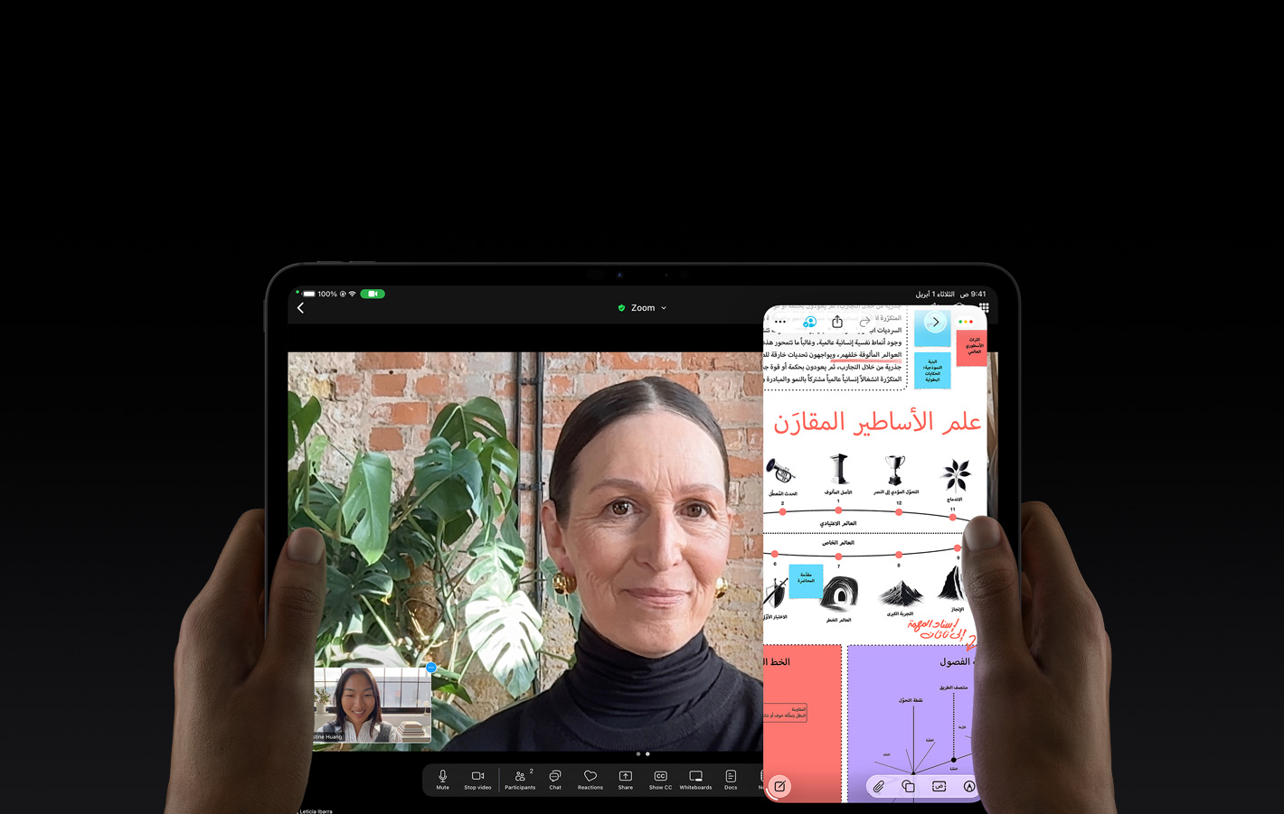 جهاز iPad Pro، الجزء الأمامي الخارجي، لون أسود فلكي، يدان يسرى ويمنى تحملان الجهاز في الوضع الأفقي، زوايا مدورة، إطار شاشة أسود، واجهة تعرض محادثة فيس تايم تُترجم مباشرةً، وتطبيق تعليمي يُظهر عرضاً تقديمياً عن 