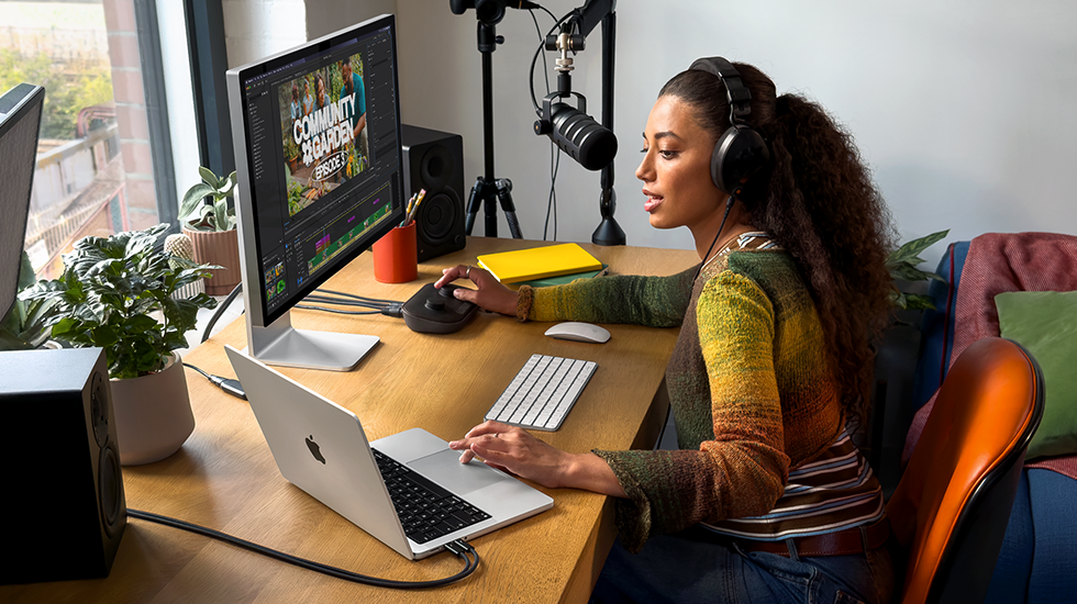 امرأة في منزلها تعمل خلف مكتبها على MacBook&nbsp;Pro متصل بشاشة خارجية وتستخدم سماعات رأس وتتحدث في الميكروفون