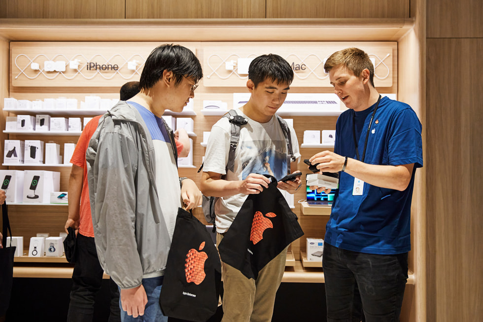 Un dipendente Apple che assiste alcuni clienti con l’acquisto di un iPhone 14 a Apple Battersea.