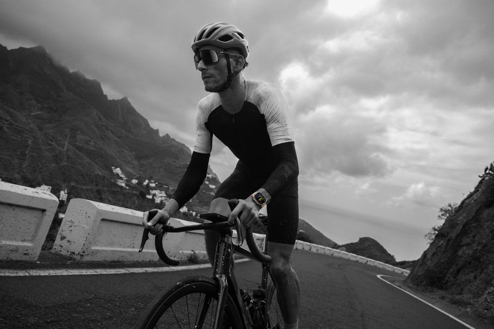 A cyclist is shown riding a bike outdoors and wearing Apple Watch Ultra 2.