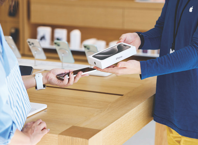 An image representing Apple Trade In shows a customer exchanging their old iPhone for a new one in a box.