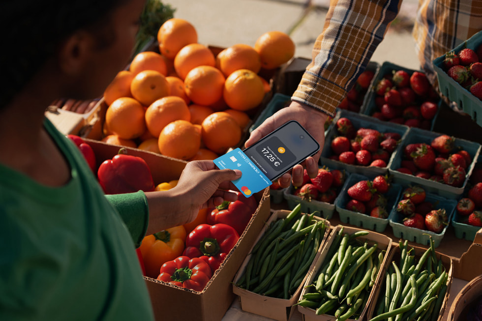 Una persona che avvicina il proprio iPhone a quello dell’esercente per completare la transazione al mercato agricolo.