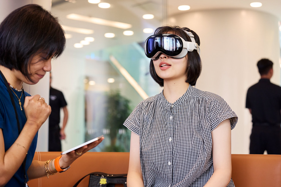 An Apple team member sits with a customer wearing Apple Vision Pro.