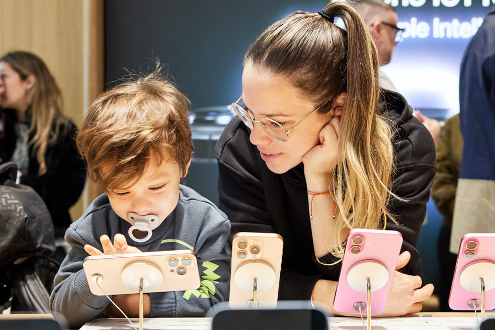 A toddler and parent examine the iPhone 16 lineup at Apple Miami Worldcenter.