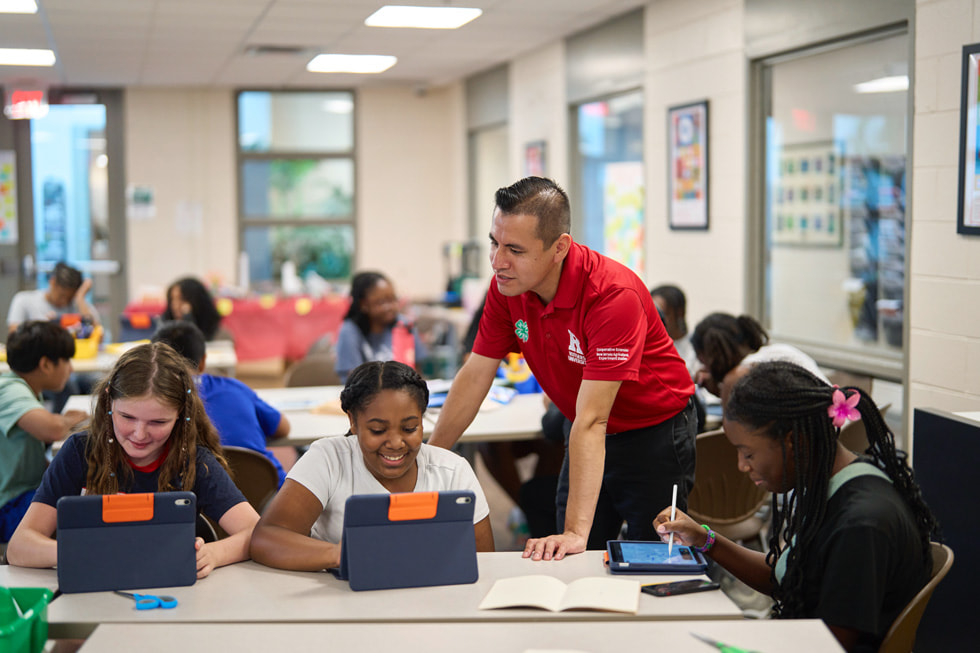 A 4-H instructor works with students using iPad and Apple Pencil in a classroom setting.
