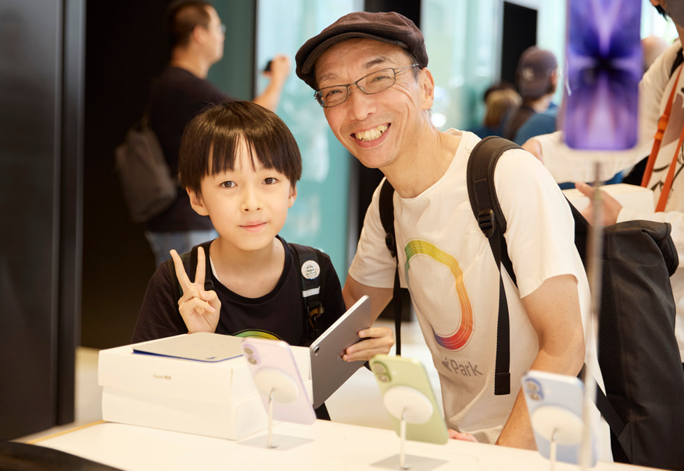 A child and adult pose with iPad beside an iPhone 17 display at Apple Ginza.