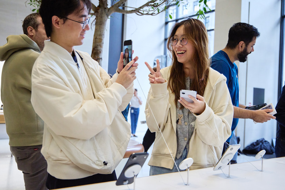 A customer poses for a photo while holding a cloud white iPhone Air as their friend snaps the shot with a space black iPhone Air. 