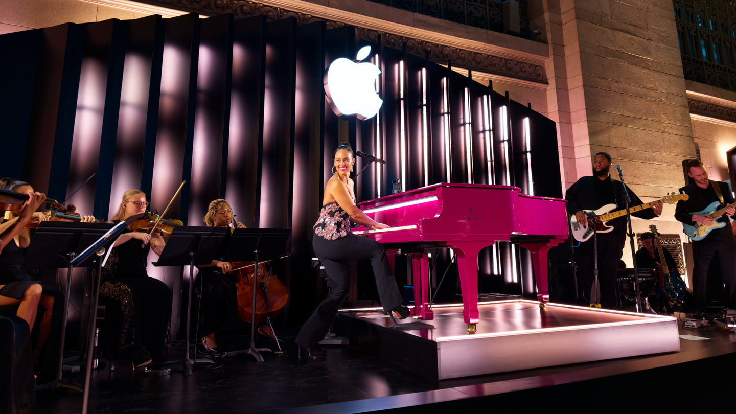 Alicia Keys plays the piano onstage at Apple Grand Central, surrounded by fellow musicians.