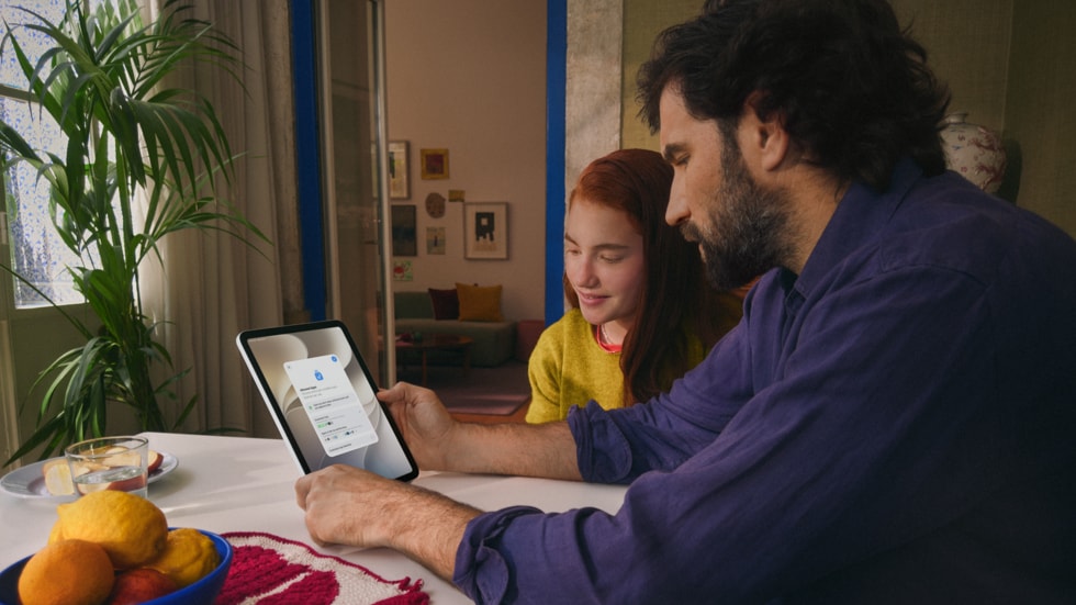 Seorang dewasa dan seorang anak duduk bersama di meja kayu, berinteraksi dengan iPad.