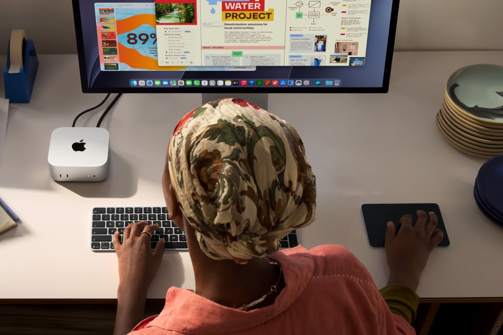 En person vist ovenfra, som bruger tastatur og mus ved et skrivebord med en Mac mini, der er tilsluttet en stor skærm.