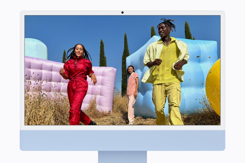 M6 çipli mavi iMac, ekranında açık havada duran üç kişinin bulunduğu bir fotoğraf gösteriliyor.
