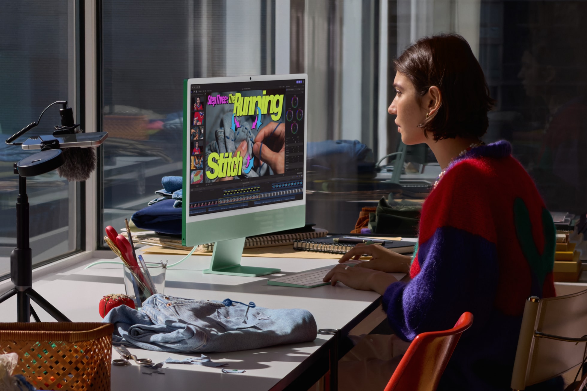 M6 çipli yeşil iMac’in önünde oturan bir kullanıcı, yanında bir dikiş projesi var ve bir video klibi düzenliyor.