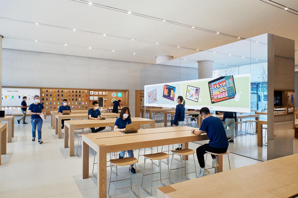 A number of display tables with customers and a freestanding video wall inside Apple Changsha.