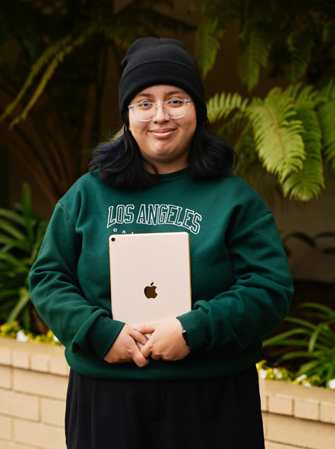 Exceptional Mindsの学生、Angela Ibarraのポートレート。Angelaは「Los Angeles, California」と書かれたグリーンのスウェットを着て、透明な眼鏡をかけ、黒いビーニー帽子をかぶっています。