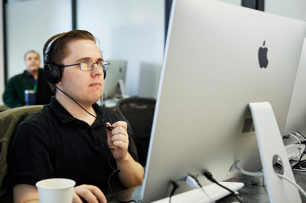 Exceptional Mindsの学生、Matthew Rohdeが学内の教室でMacを操作しているところ。Rohdeは黒のポロシャツを着てヘッドフォンをつけています。