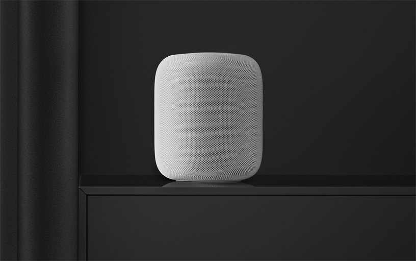 White HomePod speaker on a black shelf.
