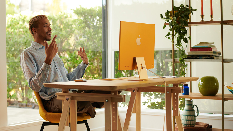 A man uses his new orange iMac, set up in his home office.