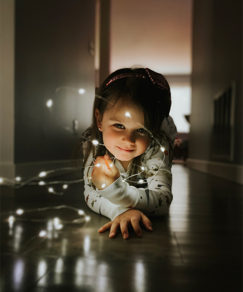 A portrait of a young girl playing with string lights.