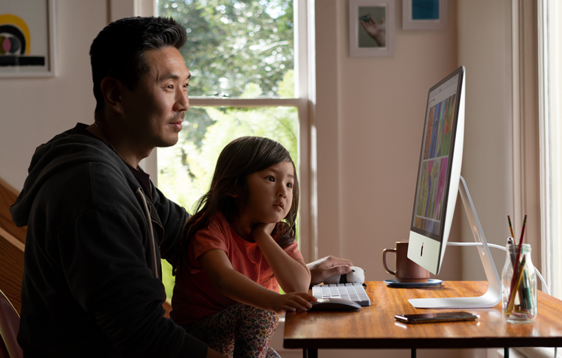 Un padre y su hija ven fotos en una iMac en su casa.