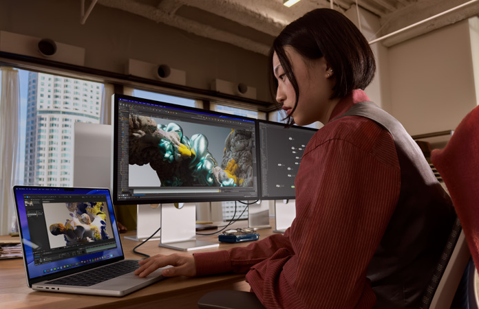 บุคคลหนึ่งขณะทำงานในออฟฟิศโดยมี MacBook Pro เชื่อมต่ออยู่กับ Studio Display XDR