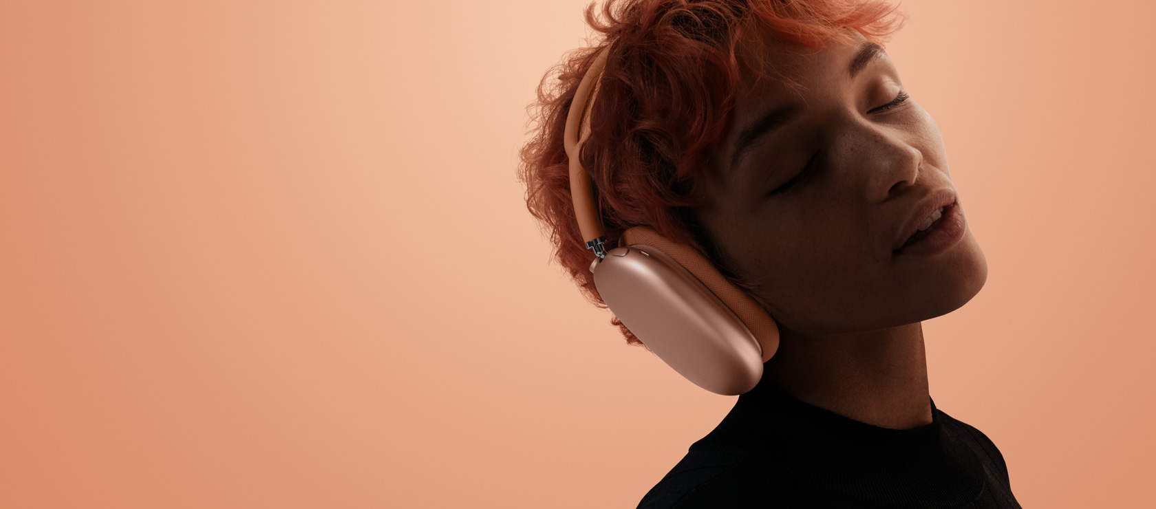Човек с наклонена глава и затворени очи, носещ AirPods Max 2, оранжев цвят, на оранжево-розов фон