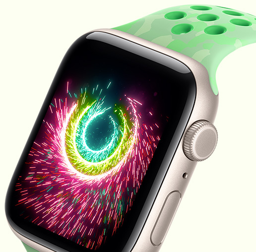 Apple Watch SE 3, på skärmen visas aktivitetsringar som gnistrar som fyrverkerier, aluminiumboett i färgen stjärnglans, Nike-sportband i färgen Green Spark (mintgrön, diskret mönster med grå former och runda hål)
