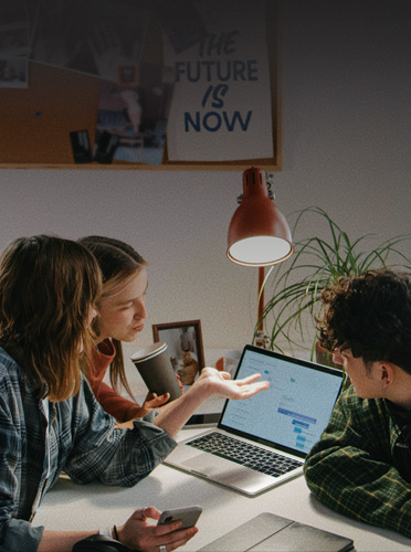 Tres estudiantes trabajan alrededor de una MacBook Pro abierta, muestra cómo el contar con dispositivos conocidos facilita la transición al mundo laboral