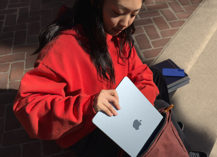 一個人坐在石階上，將 MacBook 放入背包中
