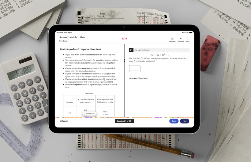 Ein iPad liegt auf einem Schreibtisch neben Prüfungsformularen aus Papier und Schulmaterial. Auf dem Bildschirm werden Anweisungen zum Lösen des mathematischen Teils eines standardisierten Tests angezeigt.