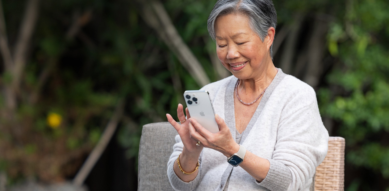 An elderly woman looking at an iPhone while sitting in a chair.