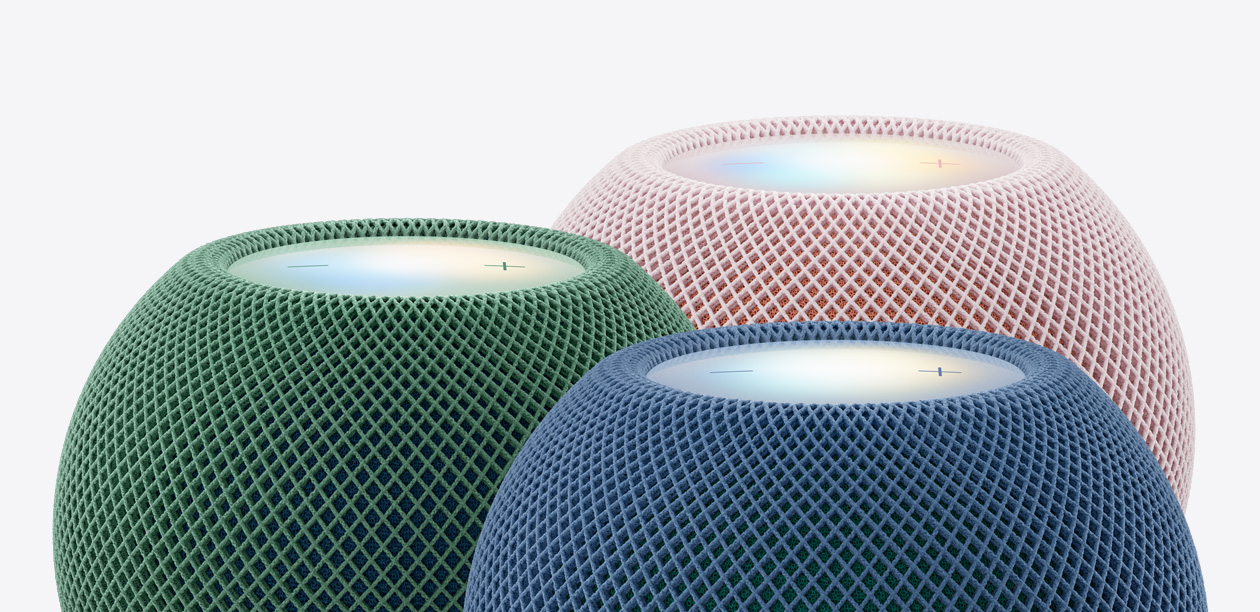 Tre HomePod mini-høyttalere i grønn, blå og rosa farge vist tett på ovenfra, med vevet nettingmateriale og lyssatte berøringsflater.