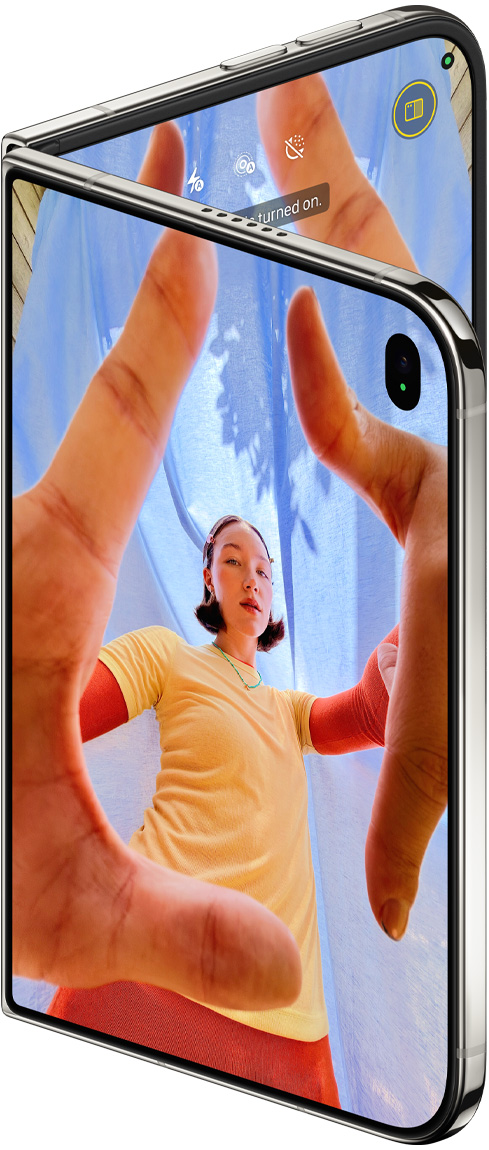少し開いたスターホワイトのiPhone Duo。センターフレームフロントカメラを備えたアウターディスプレイにはカメラアプリが表示され、インナーディスプレイには写真アプリのライブラリが表示されている
