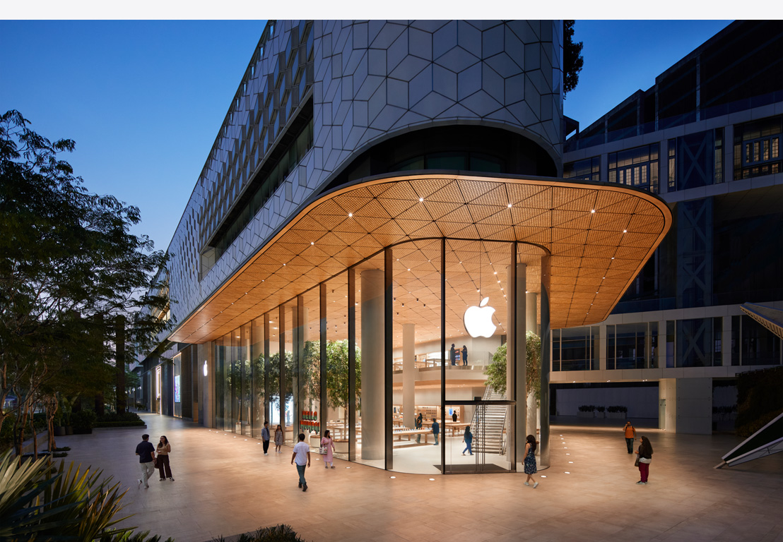 Apple Store de noche, ventanas de vidrio, interior de la tienda iluminada, logo de Apple centrado en la parte superior de la puerta de entrada