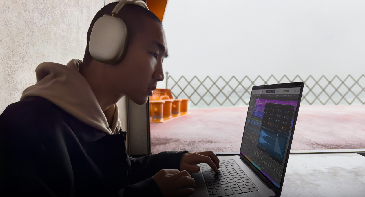Tampak samping seseorang yang mengenakan AirPods Max sedang menggunakan Logic Pro di MacBook Pro 16