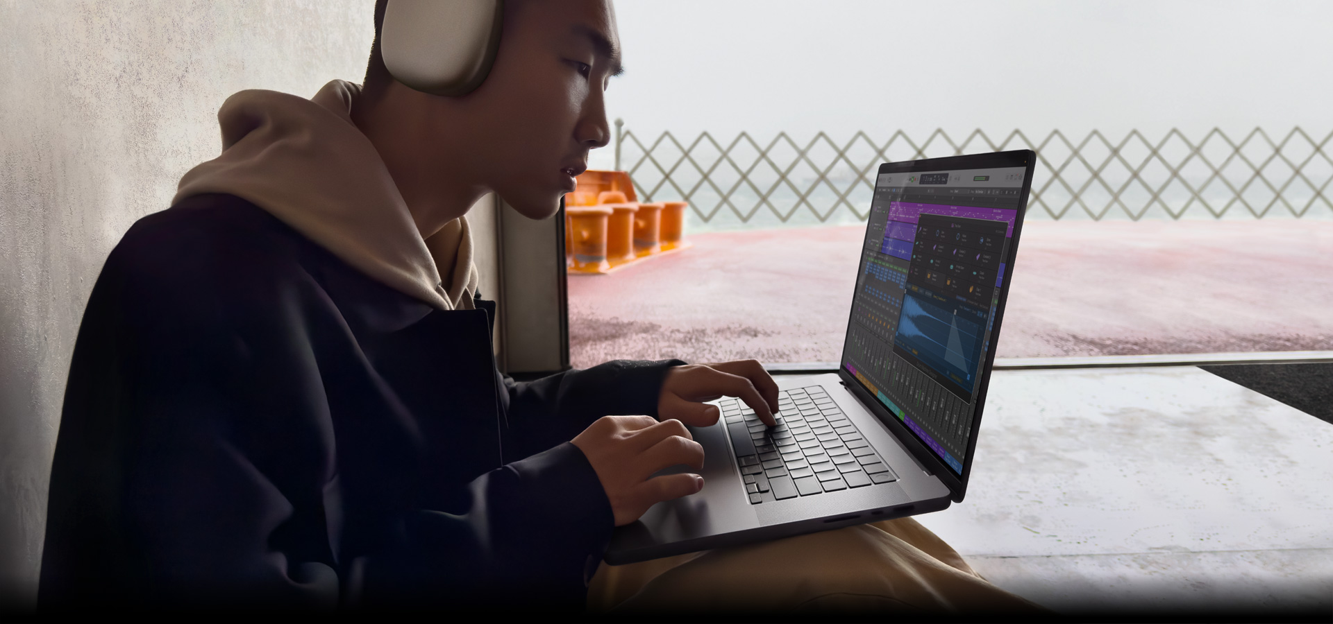 Tampak samping seseorang yang mengenakan AirPods Max sedang menggunakan Logic Pro di MacBook Pro 16, layar menampilkan ruang kerja Logic Pro