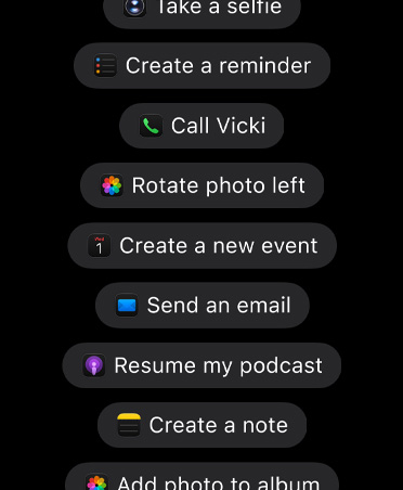 Ein Display mit Anfragen an Siri AI, um Aktionen in Apps auszuführen, darunter „Mach ein Selfie“, „Erstelle eine Erinnerung“, „Ruf Sophie an“, „Foto links drehen“, „Erstelle ein neues Event“, „Sende eine E‑Mail“, „Podcast fortsetzen“, „Erstelle eine Notiz“, „Foto zum Album hinzufügen“