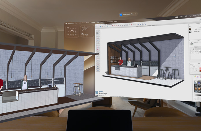Apple Vision Pro를 통해 보이는 모습. MacBook Pro가 테이블 위에 놓여 있고, 그 뒤로 3D 모델들이 투영되어 있습니다. 각 모델에는 두 사람이 서 있는 카페의 서비스 카운터가 보입니다