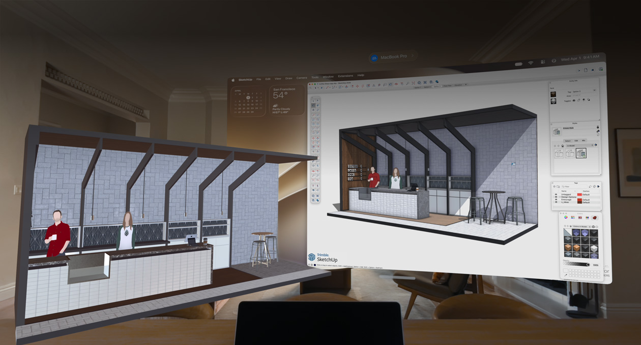 Apple Vision Pro 화면. 테이블 위에 MacBook Pro가 놓여 있고, 그 뒤로 3D 모델이 표시되어 있습니다. 3D 모델에는 카페 서비스 카운터와 그 뒤에 서 있는 두 사람이 보입니다.