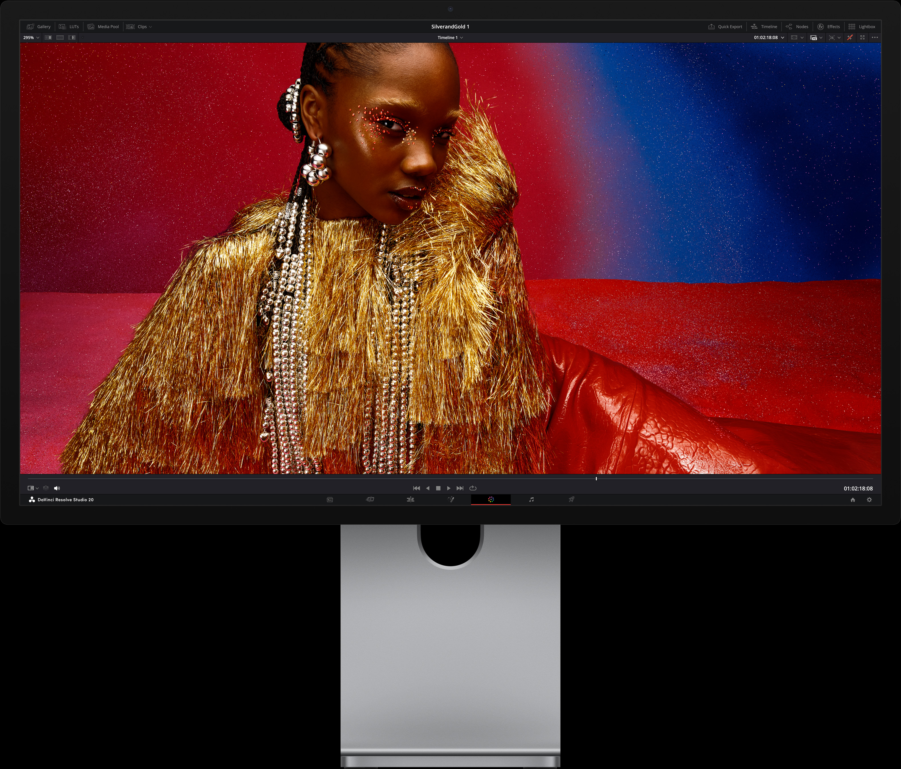 Une personne portant une robe rouge vif et des accessoires métalliques imposants est assise devant un fond bleu et rouge dégradé, illustrant la qualité d’image offerte par le Studio Display XDR