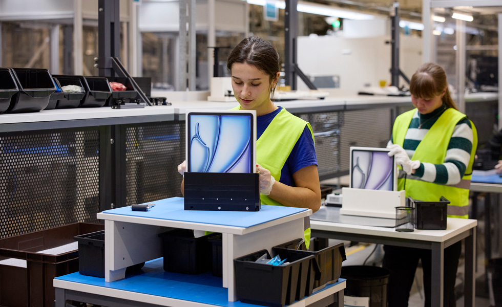 To medarbejdere i sikkerhedsveste sidder ved deres arbejdspladser med produktemballage