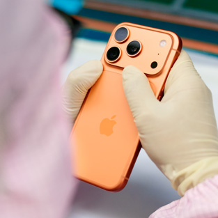 En medarbejder i fuld arbejdsdragt inspicerer en iPhone ved et arbejdsbord
