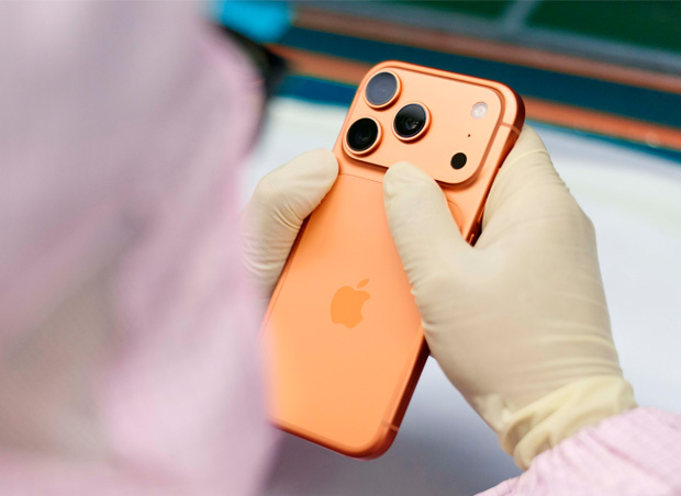 En medarbejder i fuld arbejdsdragt inspicerer en iPhone ved et arbejdsbord