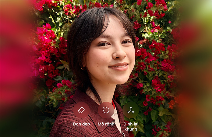 Ảnh chụp một người có mái tóc nâu, đang mỉm cười, mặc áo len nâu, xung quanh là hoa đỏ, minh họa chỉnh sửa ảnh bằng AI với các tùy chọn Dọn Dẹp, Kéo Dài, Định Lại Khung hiển thị trên ảnh